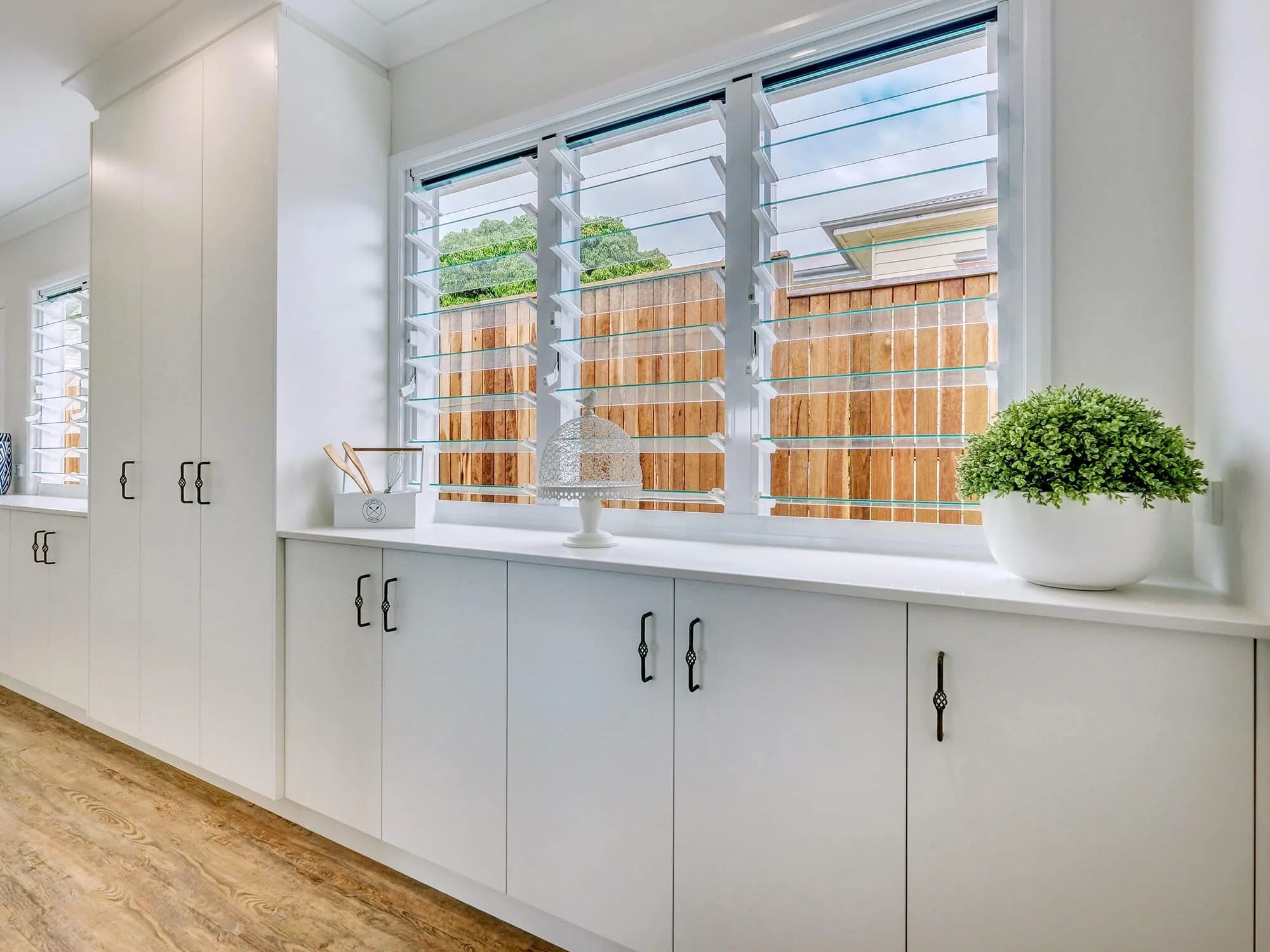 Custom laundry cabinetry with louvre windows and timber floor by MGH Cabinetmaking