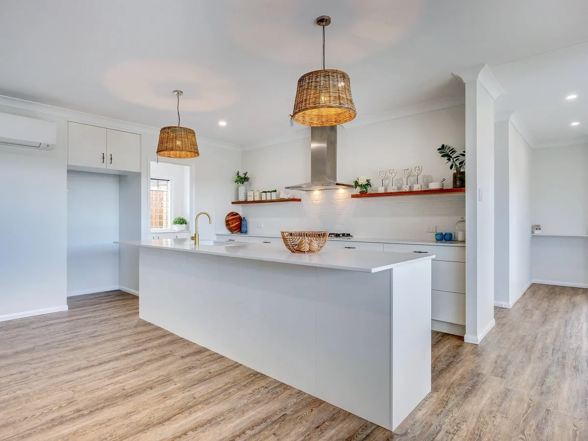Open-plan white kitchen with island and rattan pendant lights by MGH Cabinetmaking